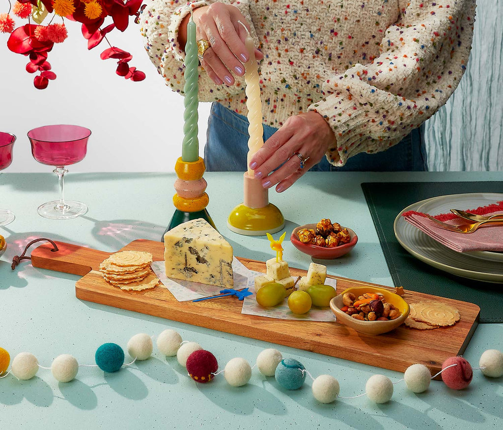 Person lighting a candle on a decorative stand with a table setting in the background