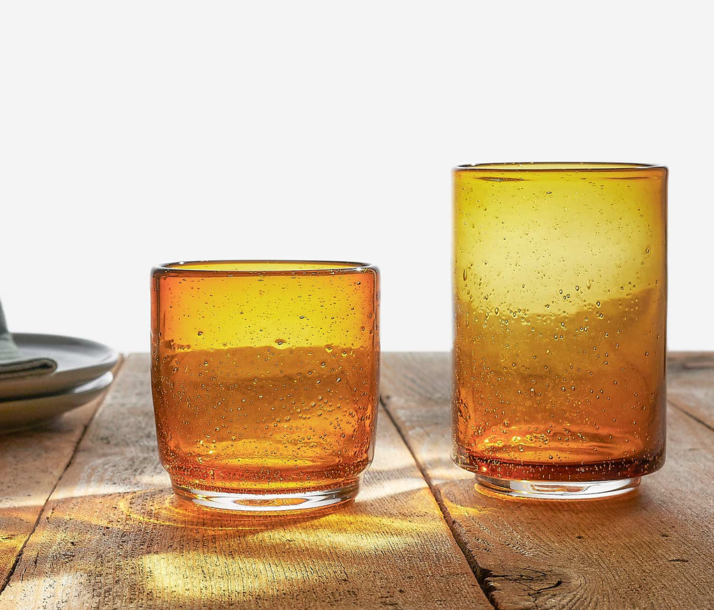 Two amber bubble glass tumblers on a wooden surface with a light background