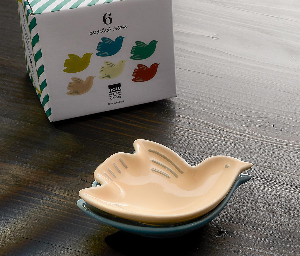 Ceramic bird-shaped dish with a box of assorted colors in the background on a wooden surface.