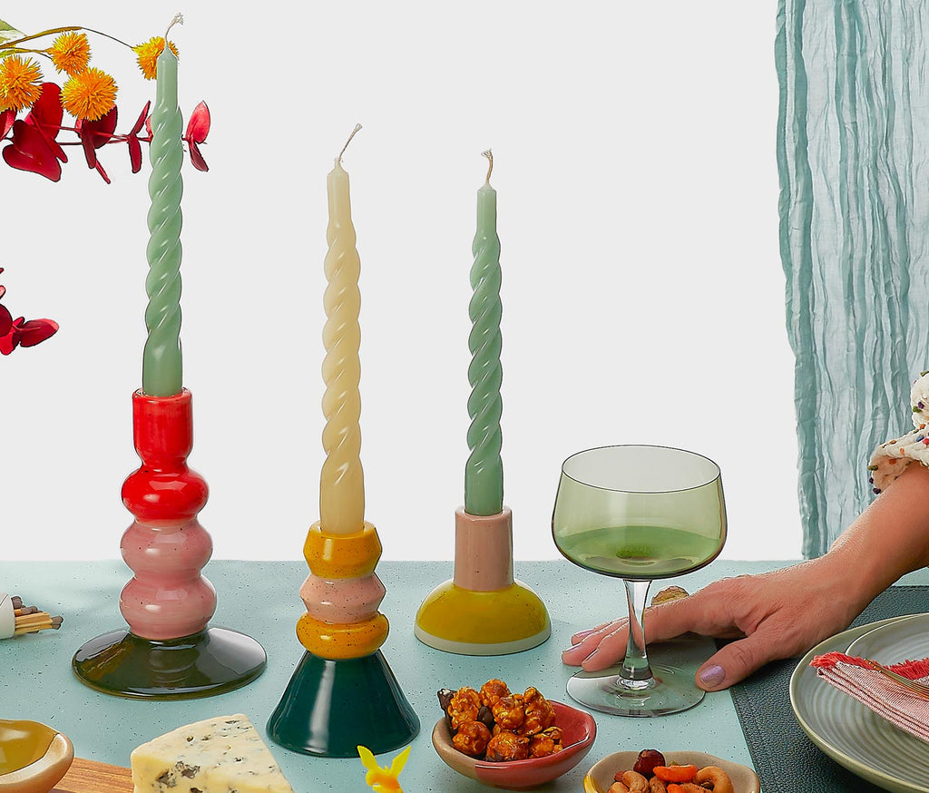 Colorful twisted candles on stands with a glass of wine and snacks on a table.