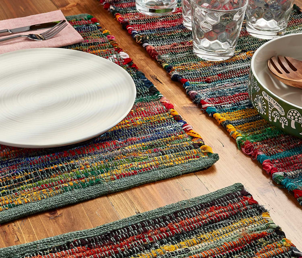 Colorful woven placemats on a wooden table with plates, glasses, and cutlery.