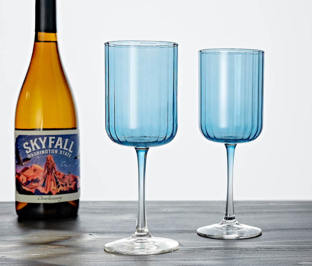 Two blue wine glasses on a wooden surface with a bottle of Skyfall Washington State wine.