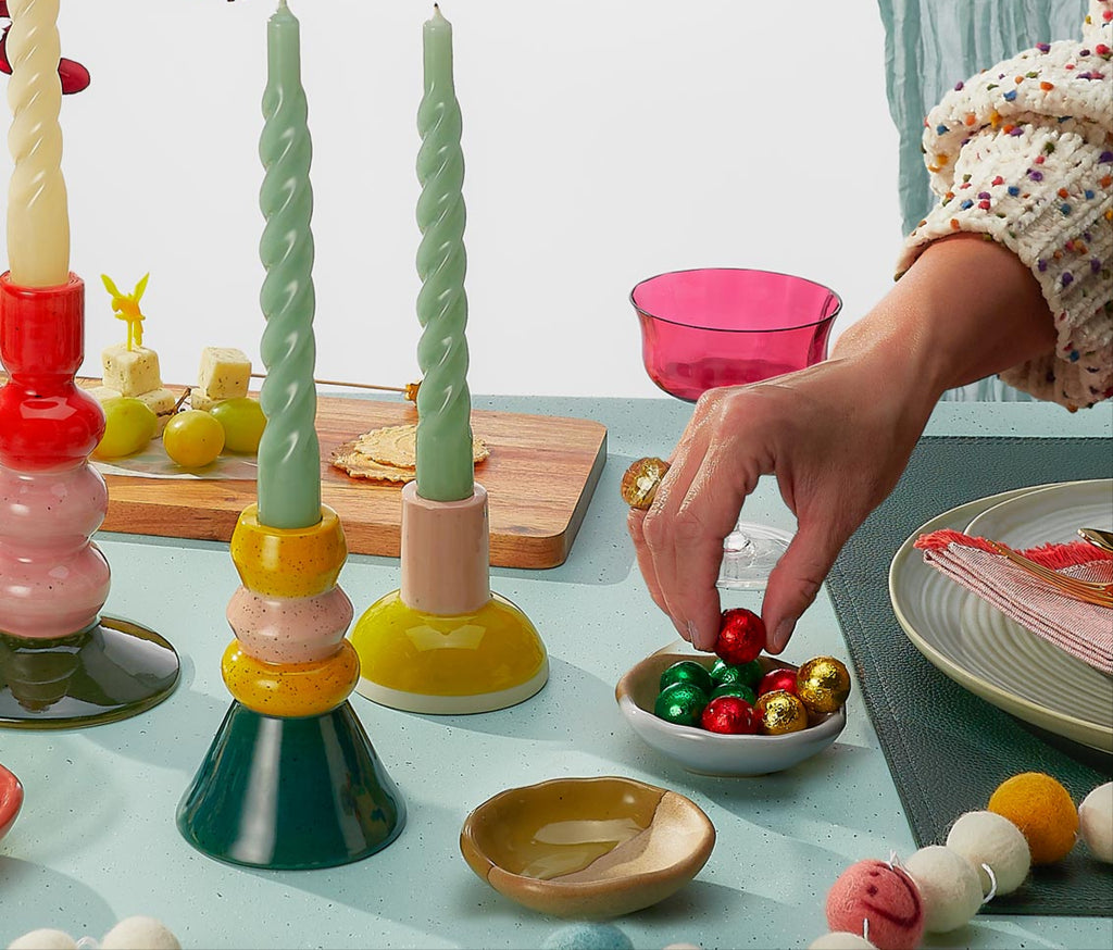 Colorful candle holders on a table with snacks and a person interacting with items.