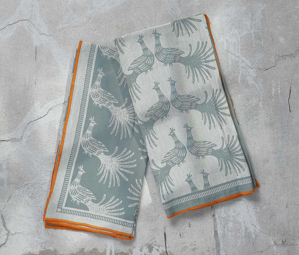 Two kitchen towels with peacock patterns on a gray surface