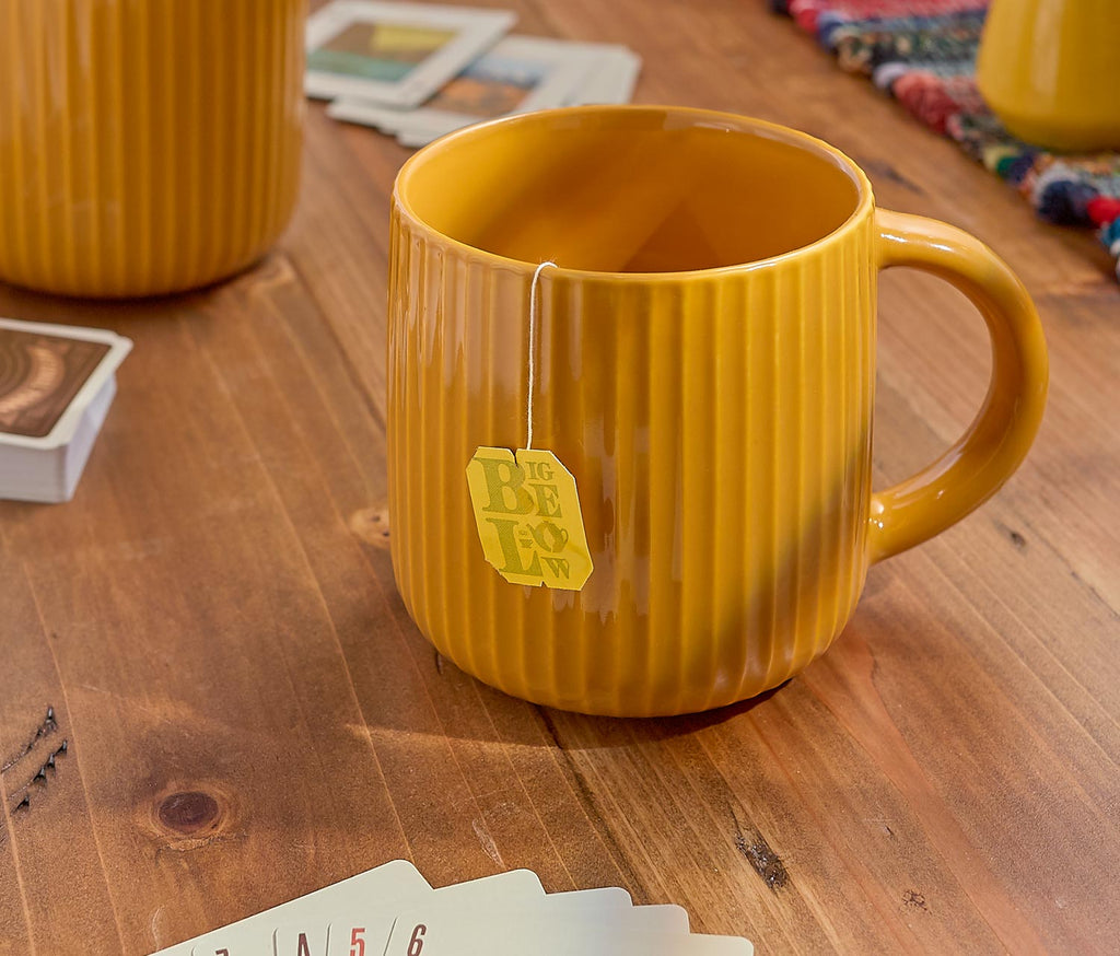 Yellow mug with a tea bag on a wooden table with playing cards.