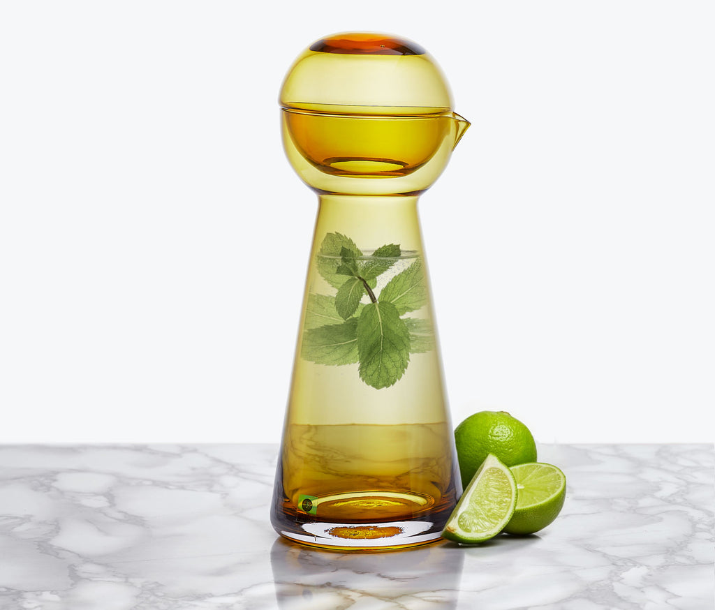 Amber-colored carafe with a lid on a marble surface with limes and mint leaves Lollygag
