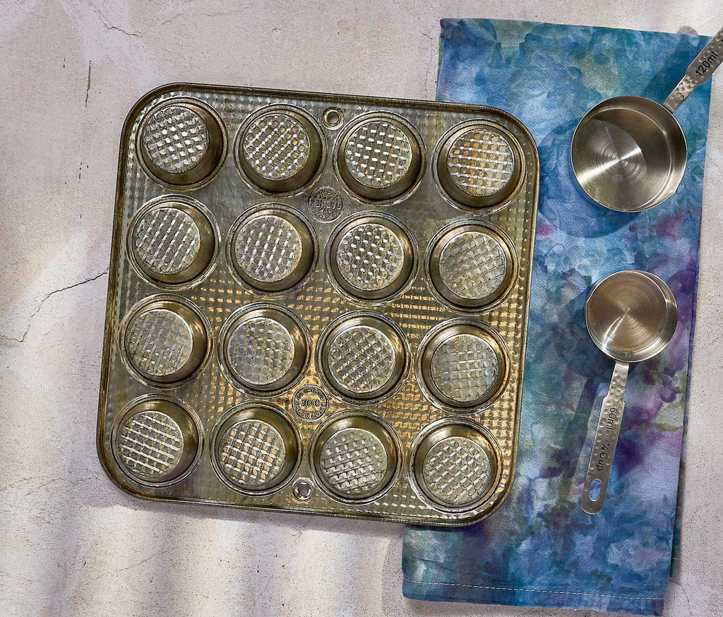 Vintage Metal muffin tin with waffle patterns on a textured surface with measuring cups.