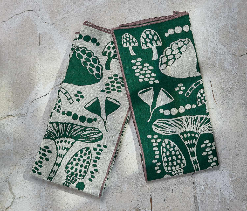 Two Mushroom  green and white patterned towels on a textured surface