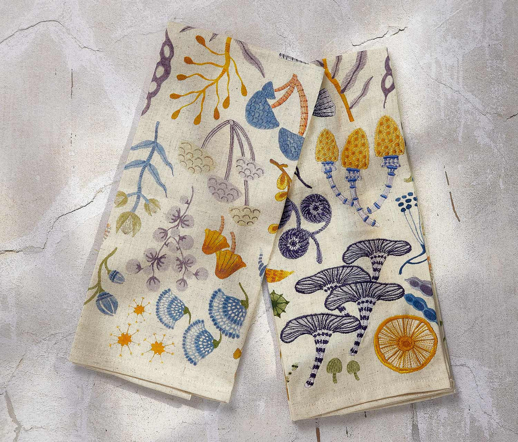 Two decorative towels with floral and mushroom patterns on a textured surface