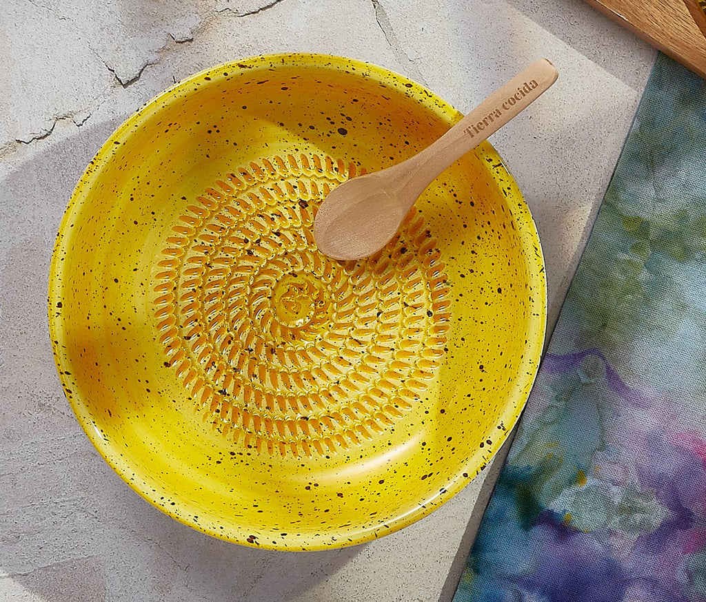 Yellow ceramic grate bowl with textured design and wooden spoon on a stone surface